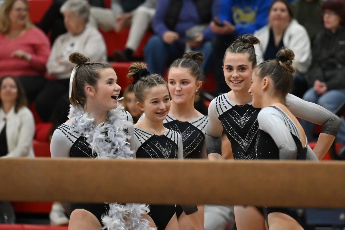 The team gathers to celebrate after Lindsay Miller performs on the beam and  Madeline Racine gets ready to compete next. 